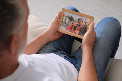 Photo of Senior man holding frame with photo of couple at home, closeup