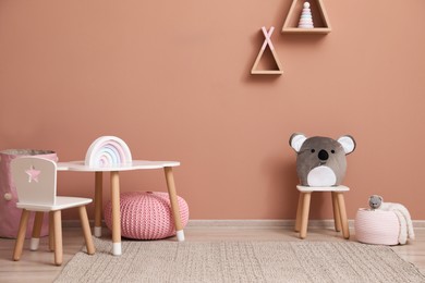 Photo of Cute child room interior with furniture, toys and wigwam shaped shelves on pink wall