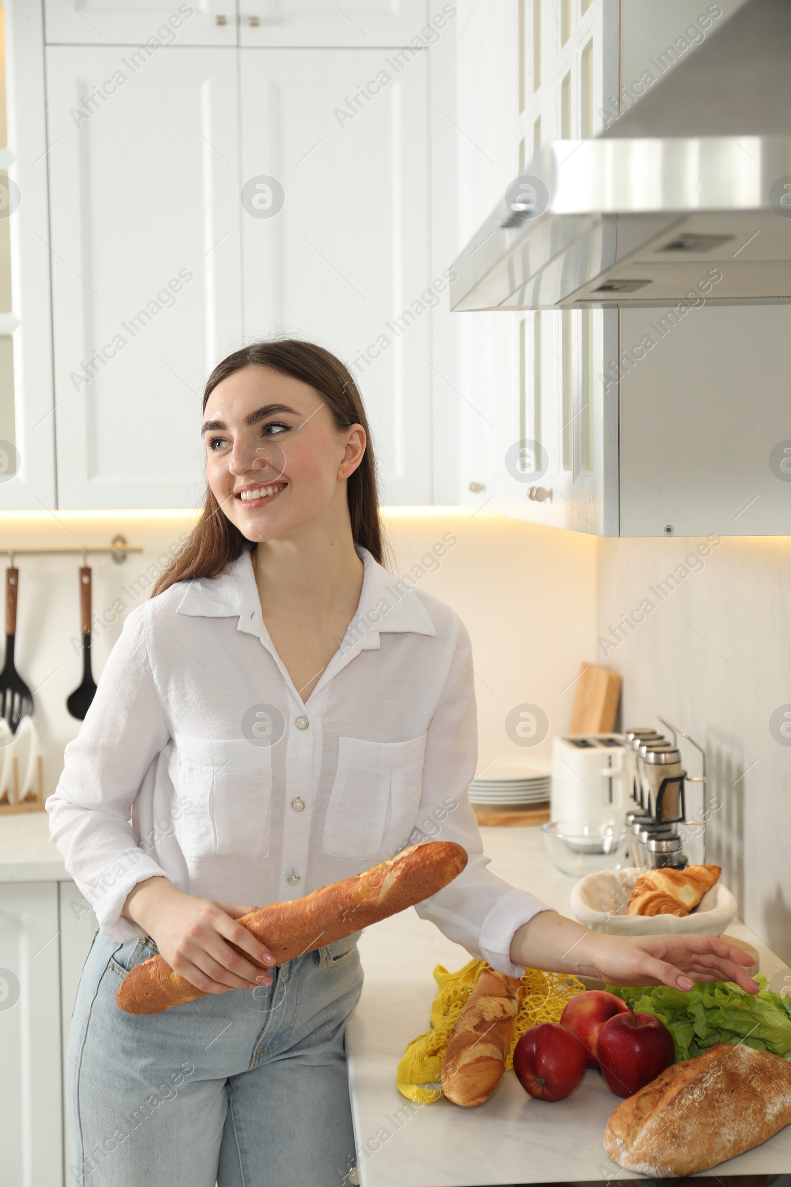 Photo of Woman with baguette and other products in kitchen