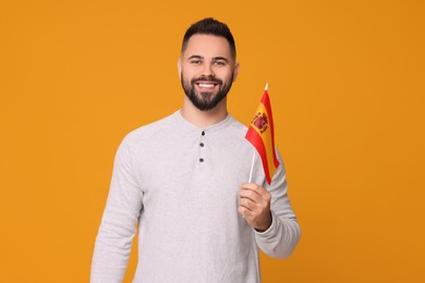 Photo of Young man holding flag of Spain on orange background