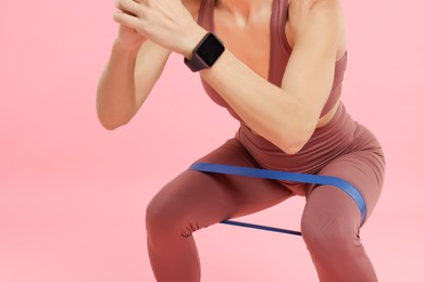 Photo of Woman exercising with elastic resistance band on pink background, closeup