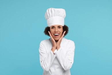 Portrait of emotional female chef in uniform on light blue background