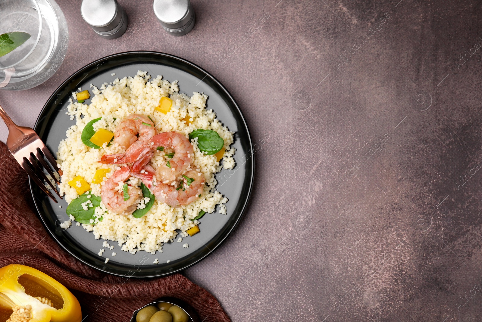 Photo of Tasty couscous with shrimps, bell pepper and basil on brown textured table, flat lay. Space for text