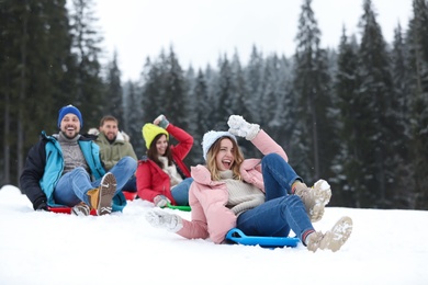 Photo of Happy friends sliding on sleds outdoors. Winter vacation
