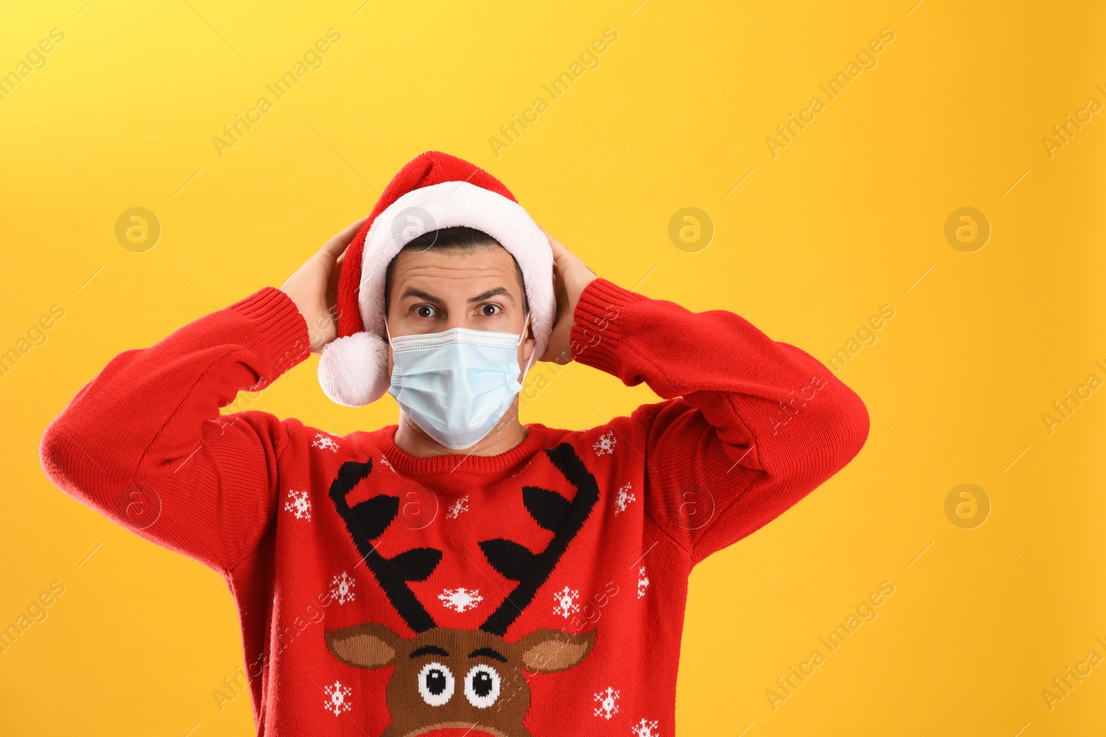 Photo of Surprised man wearing Santa hat and medical mask on yellow background