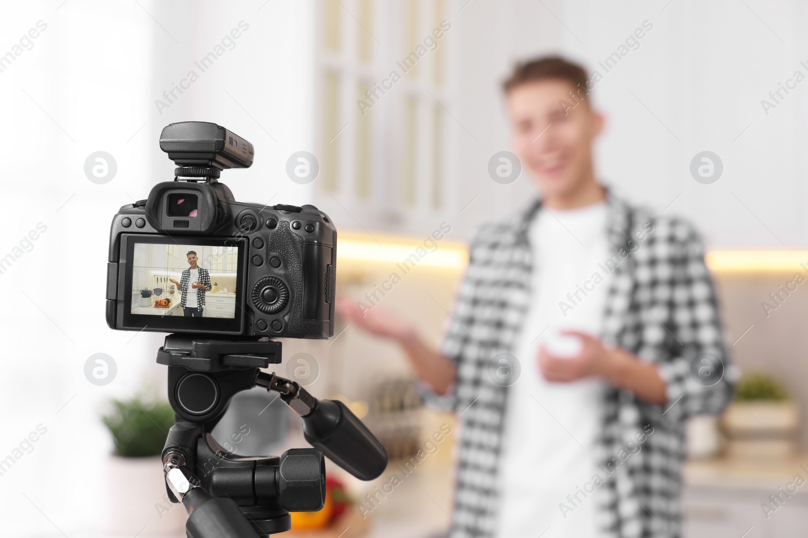Photo of Food blogger recording video in kitchen, focus on camera