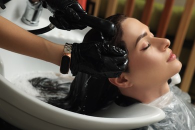 Hairdresser rinsing out dye from woman's hair in beauty salon
