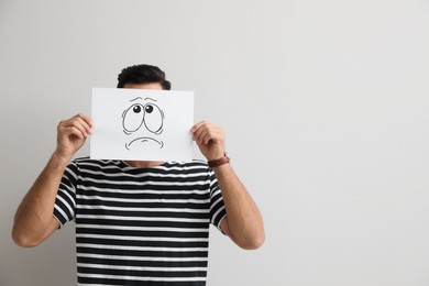 Photo of Man hiding emotions using card with drawn frowning face on white background