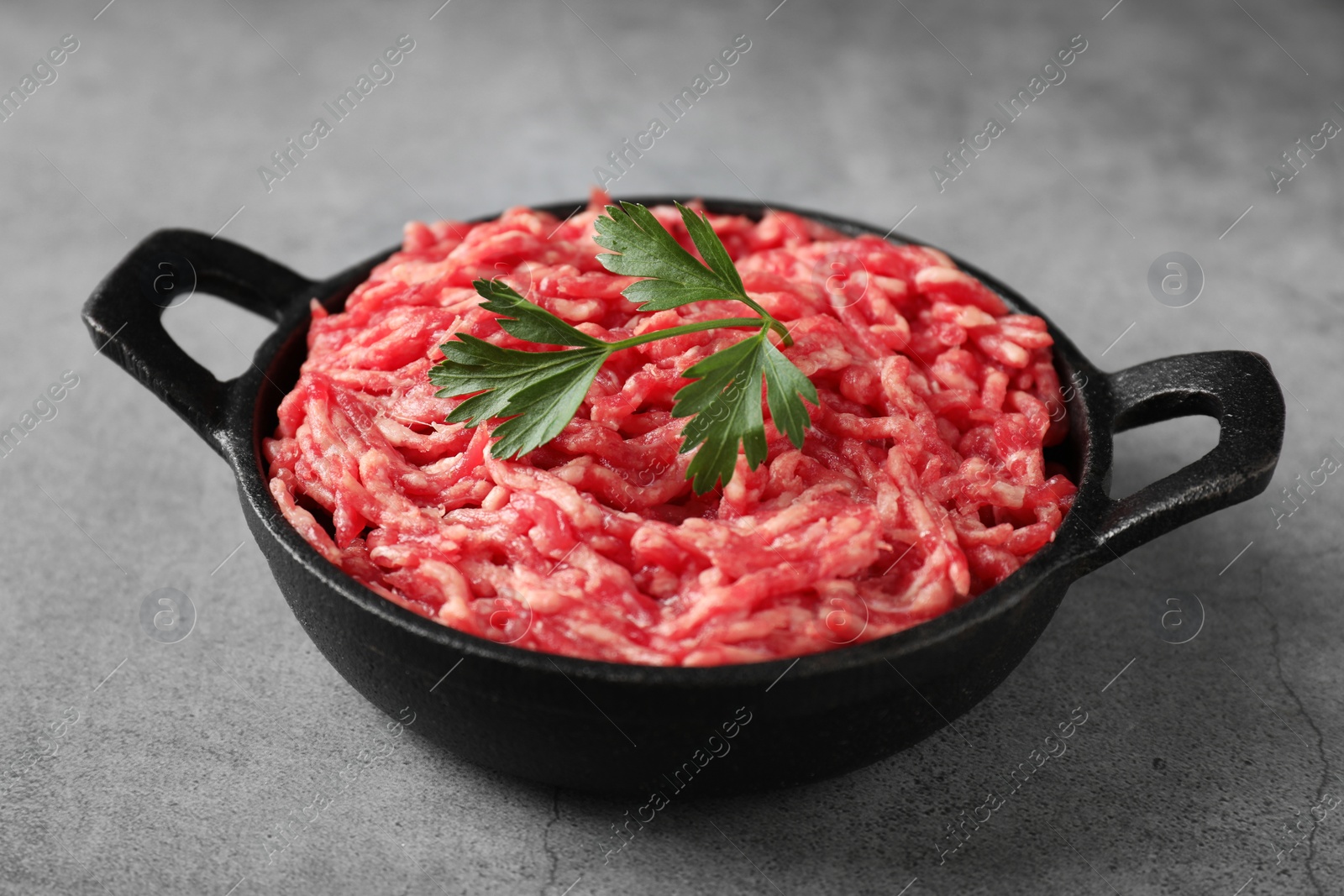 Photo of Raw ground meat and parsley in bowl on grey table, closeup