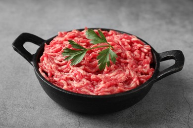 Photo of Raw ground meat and parsley in bowl on grey table, closeup