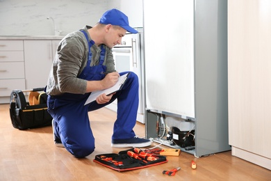 Male technician with clipboard examining refrigerator in kitchen