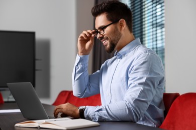 Photo of Happy young man working on laptop at table in office