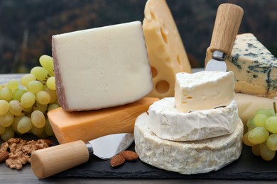 Photo of Different types of delicious cheeses and snacks on wooden table outdoors