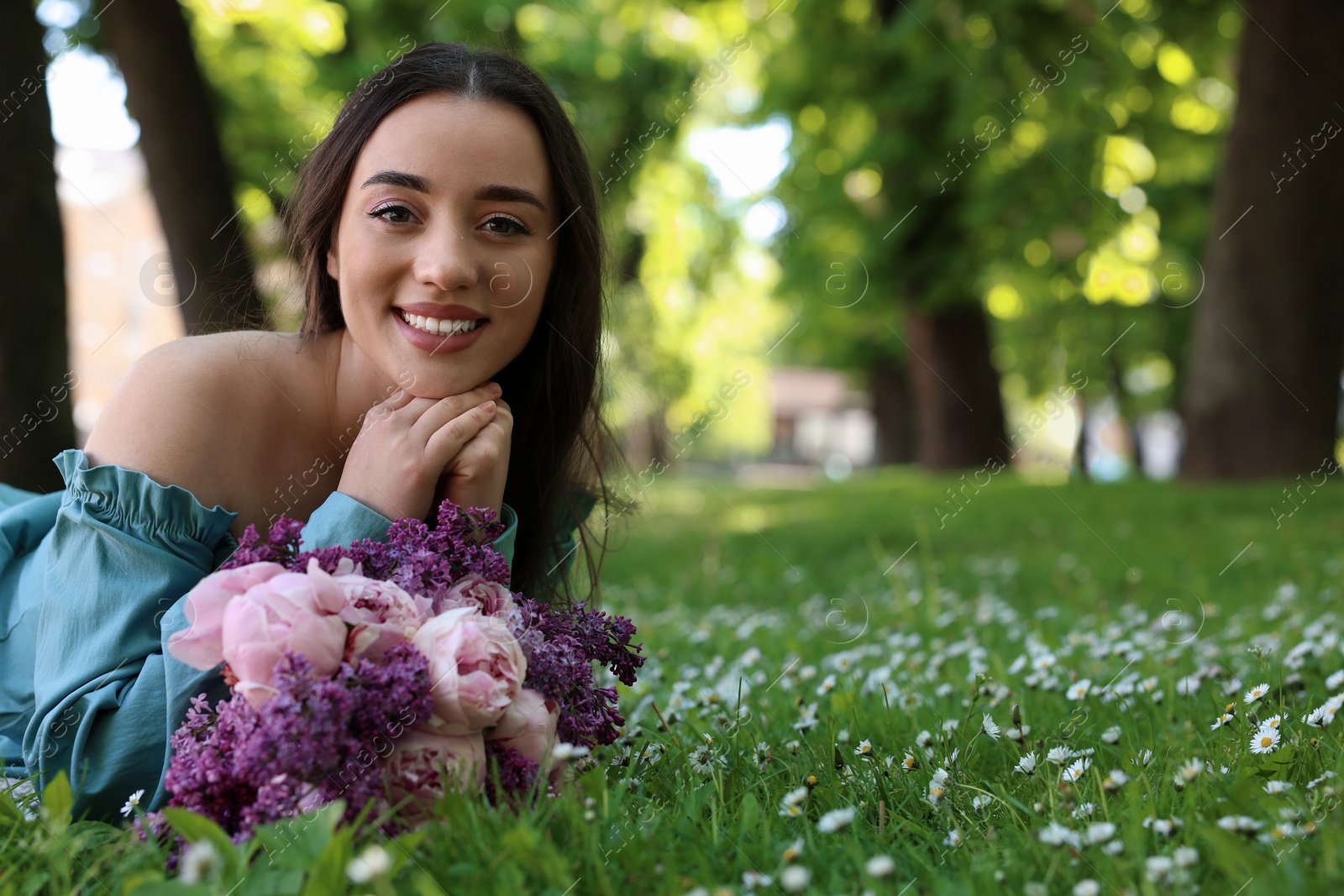 Photo of Beautiful woman with bouquet of spring flowers on green grass in park, space for text