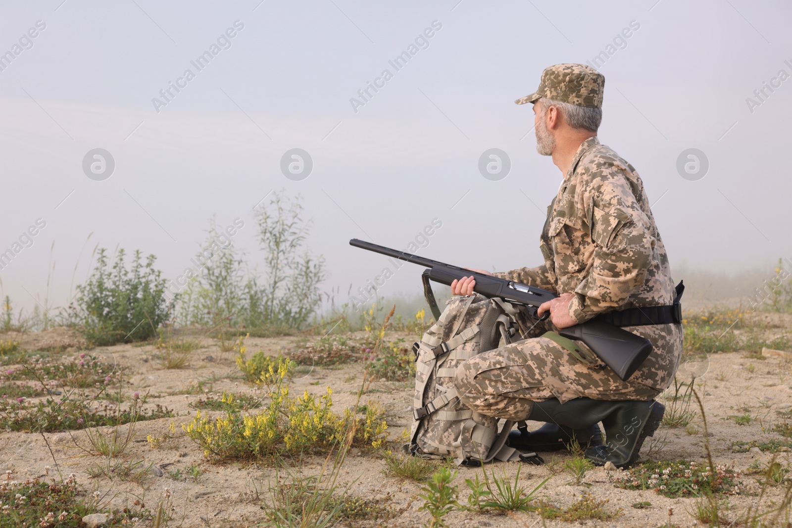 Photo of Man wearing camouflage with hunting rifle and backpack outdoors. Space for text