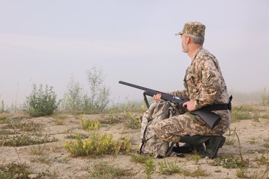 Man wearing camouflage with hunting rifle and backpack outdoors. Space for text