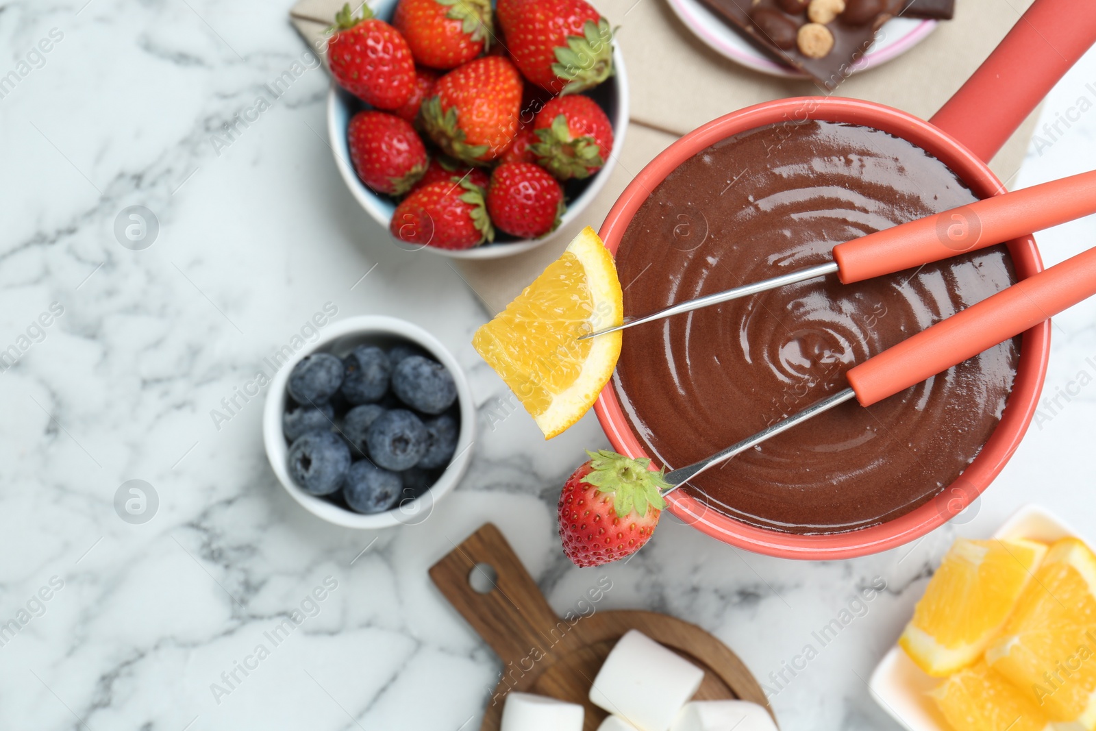 Photo of Fondue pot with melted chocolate, fresh orange, different berries and forks on white marble table, flat lay. Space for text