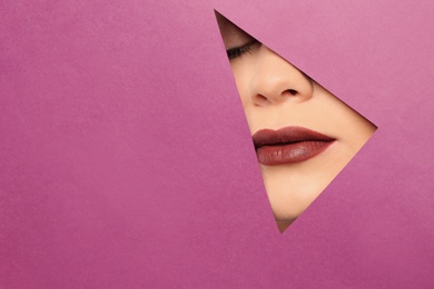Lips of beautiful young woman with dark lipstick visible through hole in color paper. Space for text