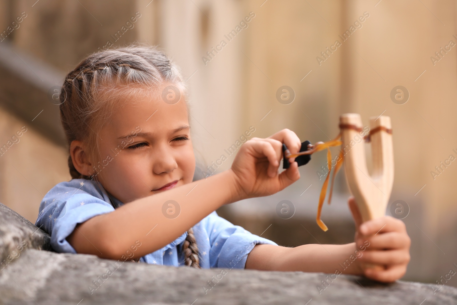 Photo of Cute little girl playing with slingshot outdoors