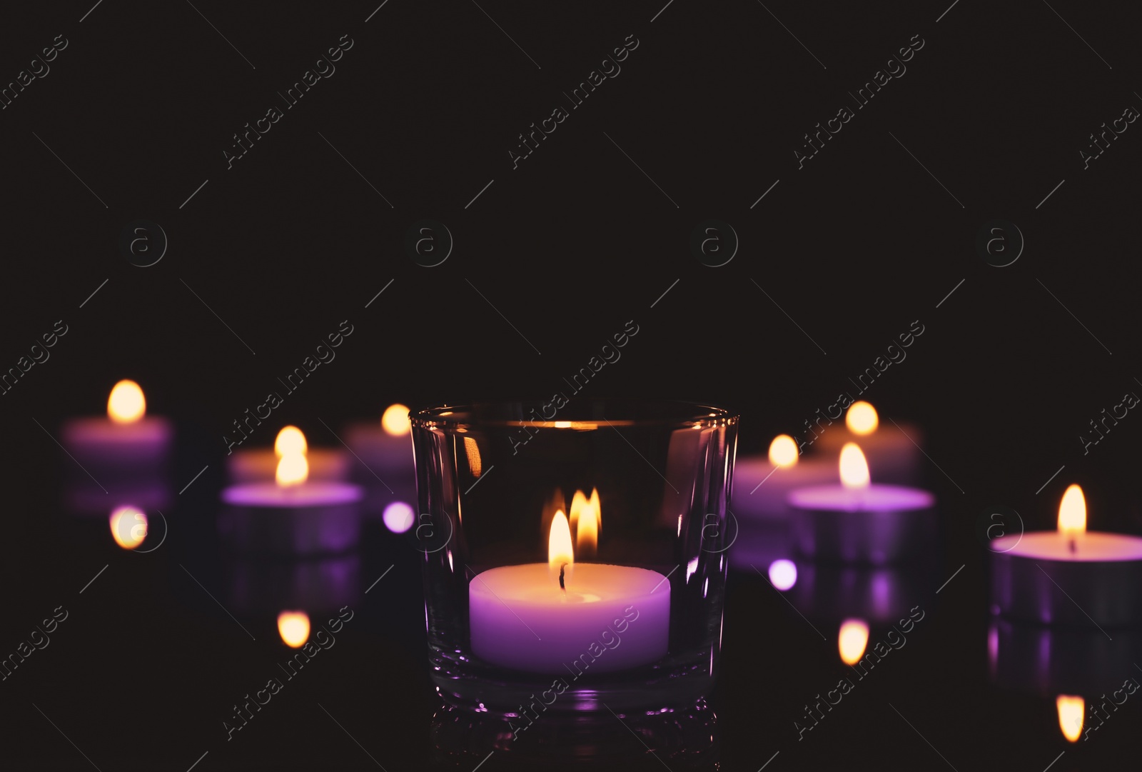 Image of Beautiful burning violet wax candles on black background. Funeral attributes