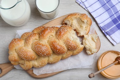 Photo of Broken homemade braided bread, milk and honey on white wooden table, flat lay. Traditional Shabbat challah