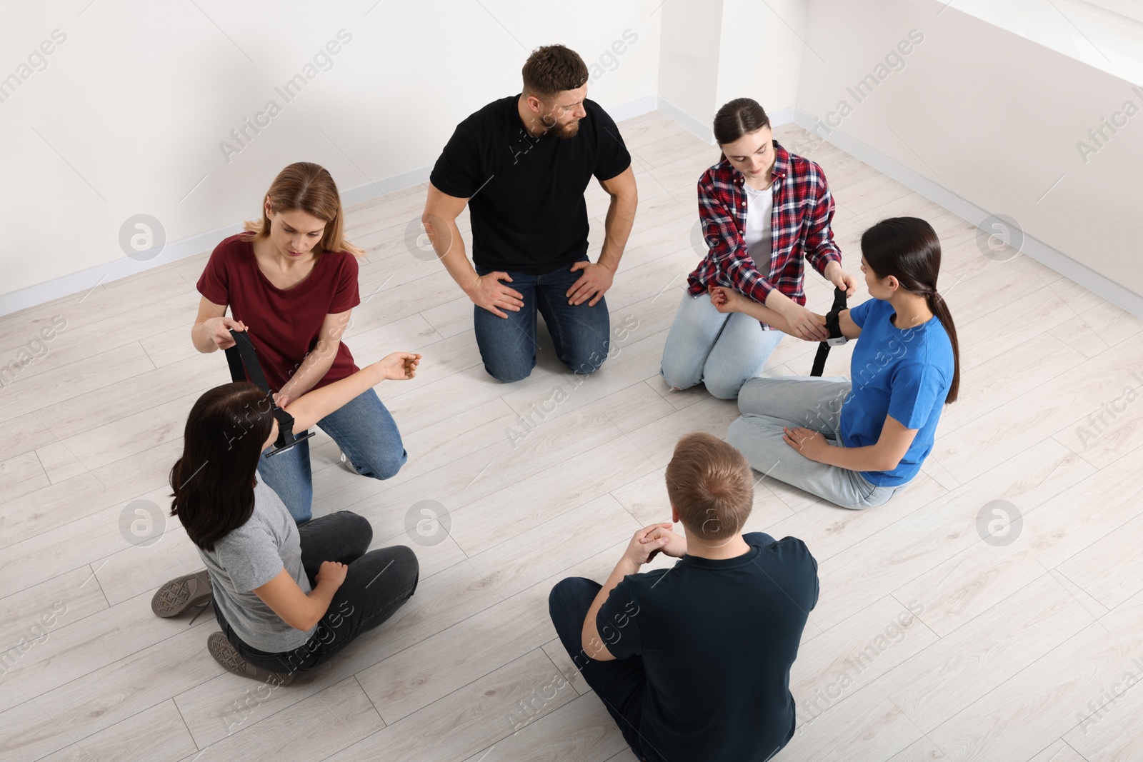 Photo of Group of people learning how to apply medical tourniquet indoors, above view