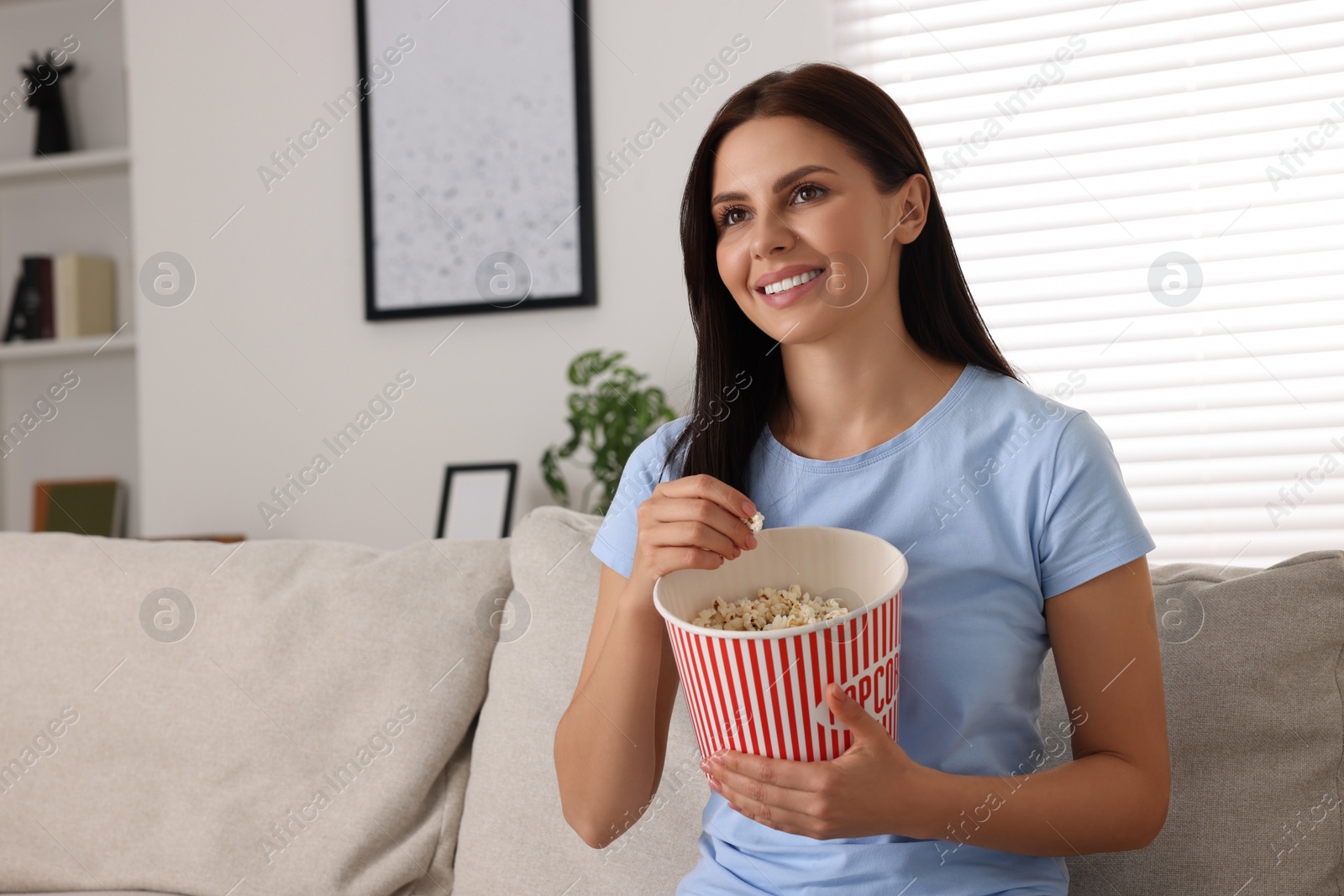 Photo of Happy woman with popcorn bucket watching TV on sofa at home