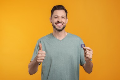 Happy man with condom showing thumb up on orange background