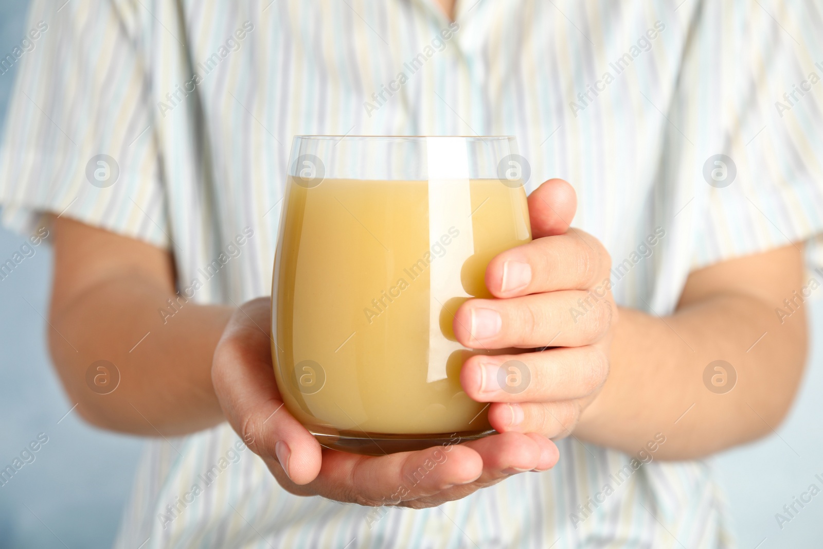 Photo of Woman holding tasty pear juice on light blue background, closeup