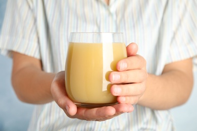 Woman holding tasty pear juice on light blue background, closeup