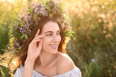 Photo of Young woman wearing wreath made of beautiful flowers outdoors on sunny day