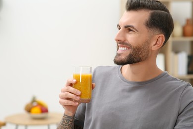 Photo of Handsome man with delicious smoothie at home. Space for text