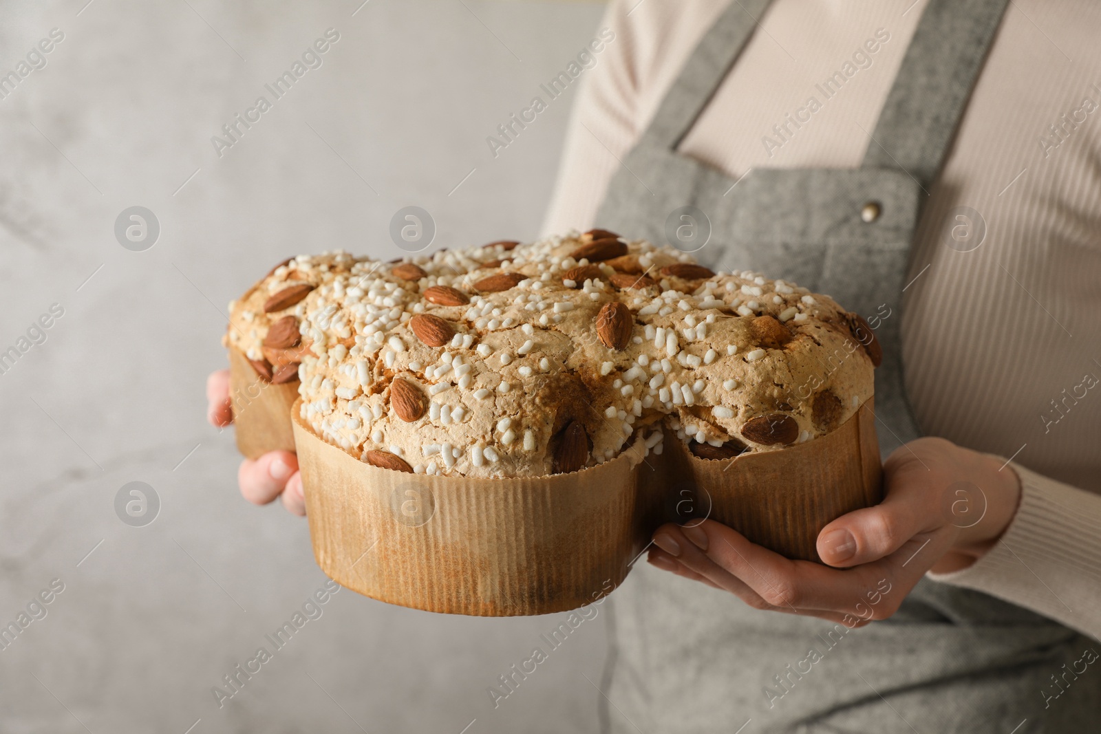 Photo of Woman with delicious Italian Easter dove cake (traditional Colomba di Pasqua) near grey wall, closeup