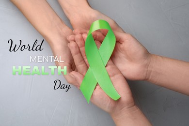 Image of World Mental Health Day. Women holding green ribbon on light grey background, top view