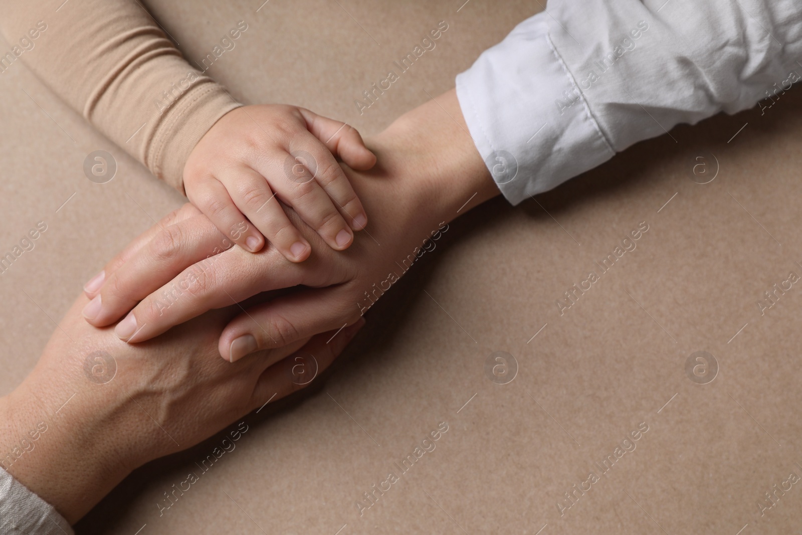 Photo of Family holding hands together on brown background, above view. Space for text