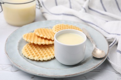 Photo of Tasty condensed milk and waffles on white textured table, closeup