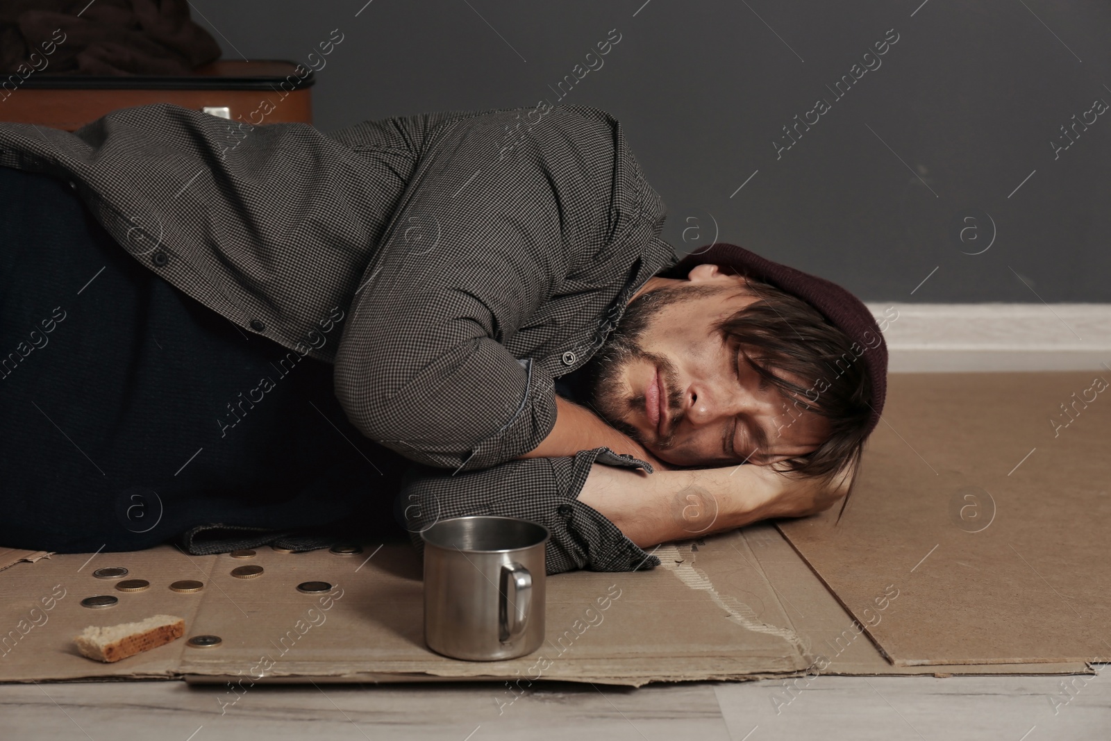 Photo of Poor homeless man sleeping on floor near dark wall