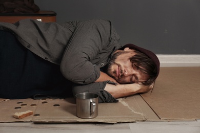 Poor homeless man sleeping on floor near dark wall