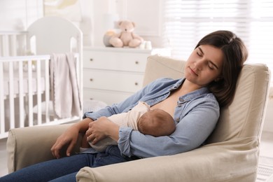 Photo of Tired young mother sleeping while breastfeeding her baby in children's room