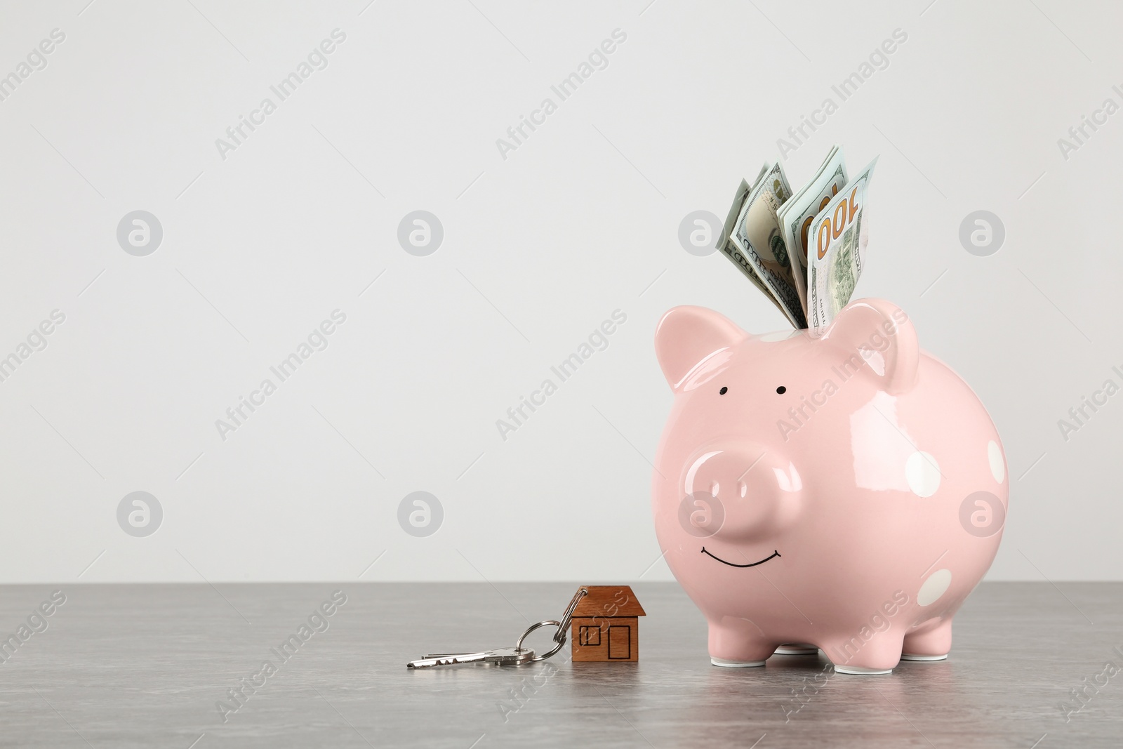 Photo of Piggy bank with dollar banknotes and house keys on table against white background. Space for text