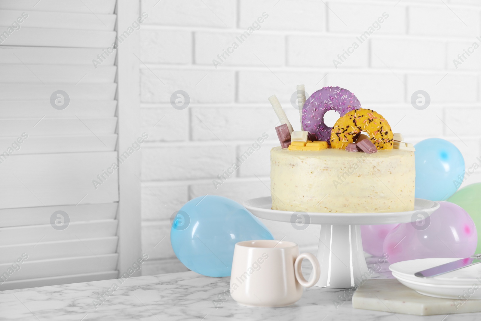 Photo of Delicious cake decorated with sweets, tableware and balloons on white marble table, space for text