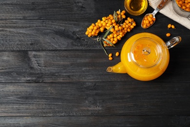 Photo of Delicious sea buckthorn tea and fresh berries on black wooden table, flat lay. Space for text