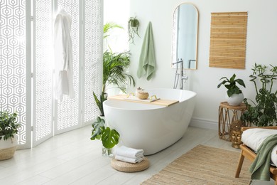 Photo of Stylish bathroom interior with modern tub, houseplants and beautiful decor. Home design