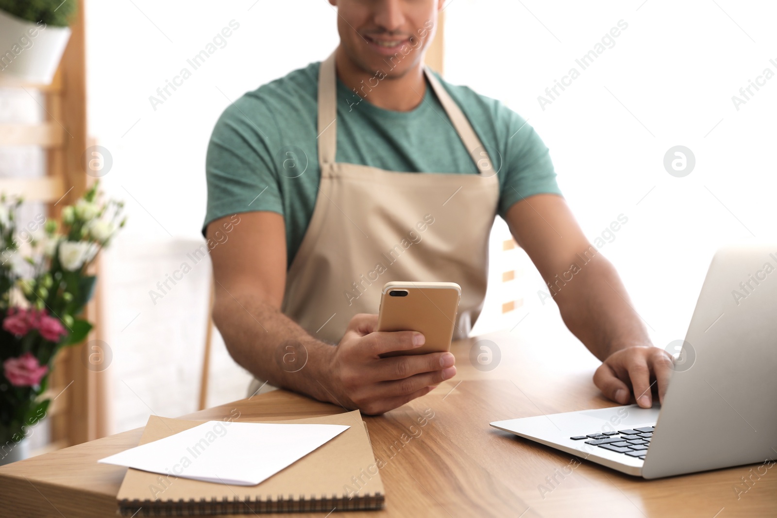 Photo of Florist with smartphone working on laptop in store, closeup