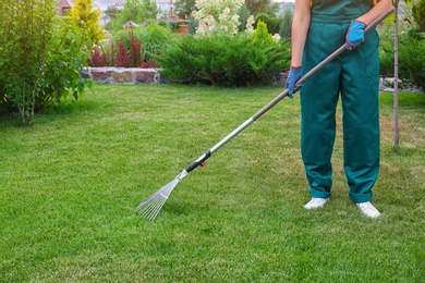 Photo of Woman raking green lawn at backyard. Home gardening
