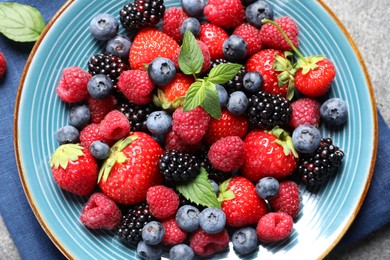 Many different fresh ripe berries in plate on grey table, top view