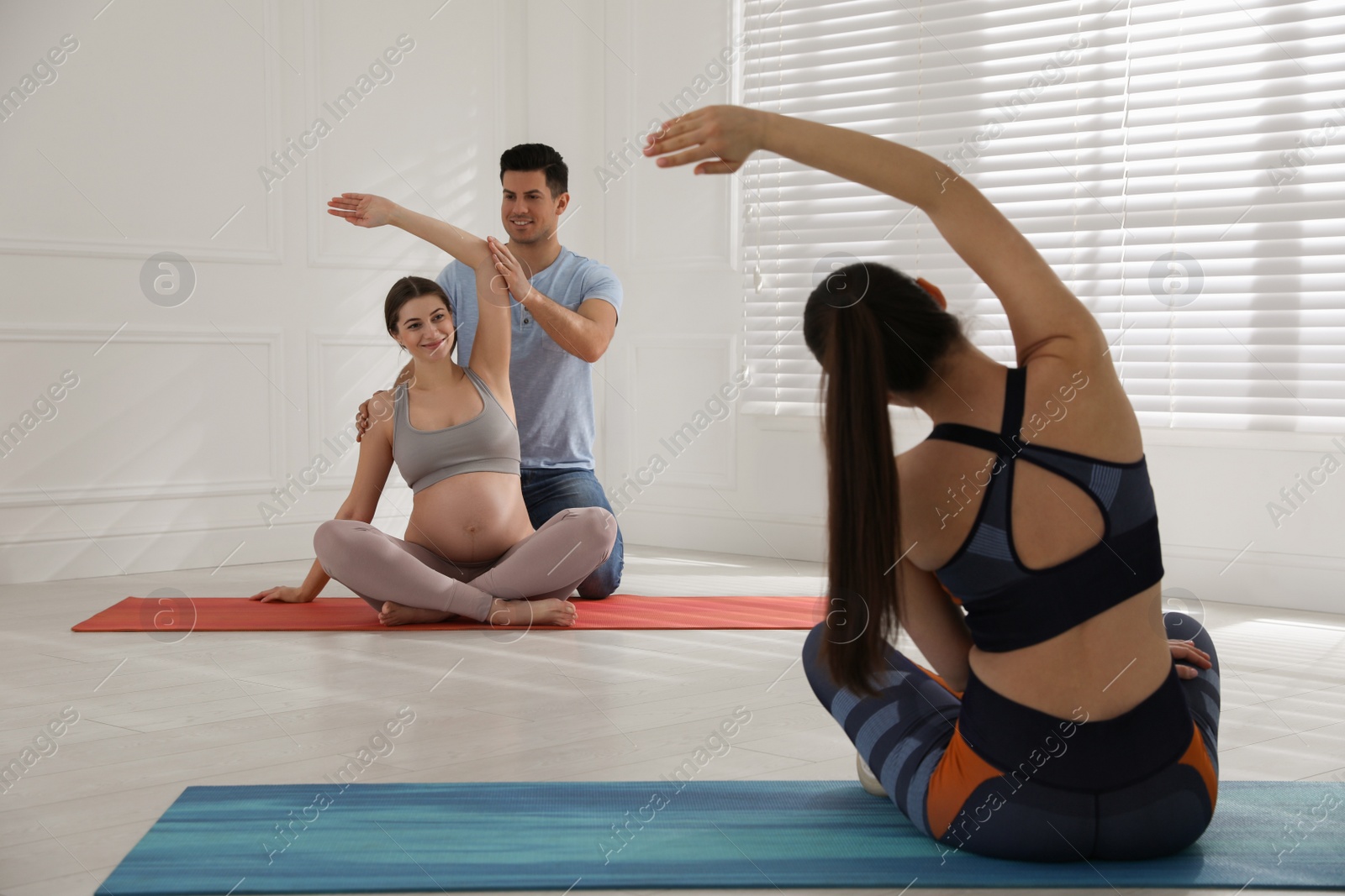 Photo of Pregnant woman and her husband working with trainer in gym. Preparation for child birth
