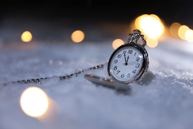 Photo of Pocket watch and Christmas lights on white snow outdoors, space for text. Midnight countdown