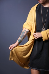 Photo of Trendy young woman with tattoo on grey background, closeup