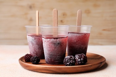 Photo of Tasty blackberry ice pops in plastic cups on white table. Fruit popsicle